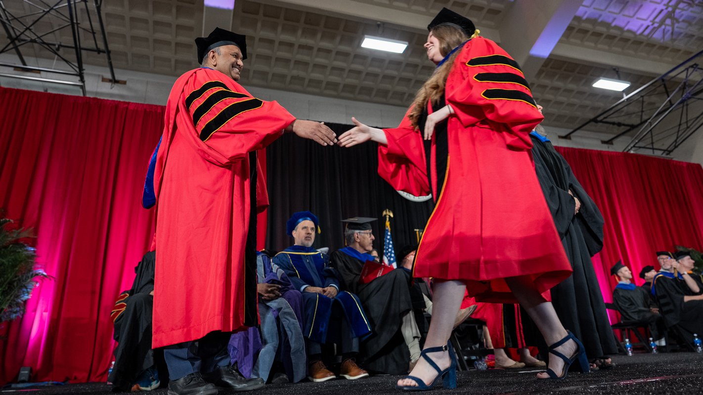 A femail Ph.D. student crossing the stage to shake the Dean Amitabh Varshney's hand.