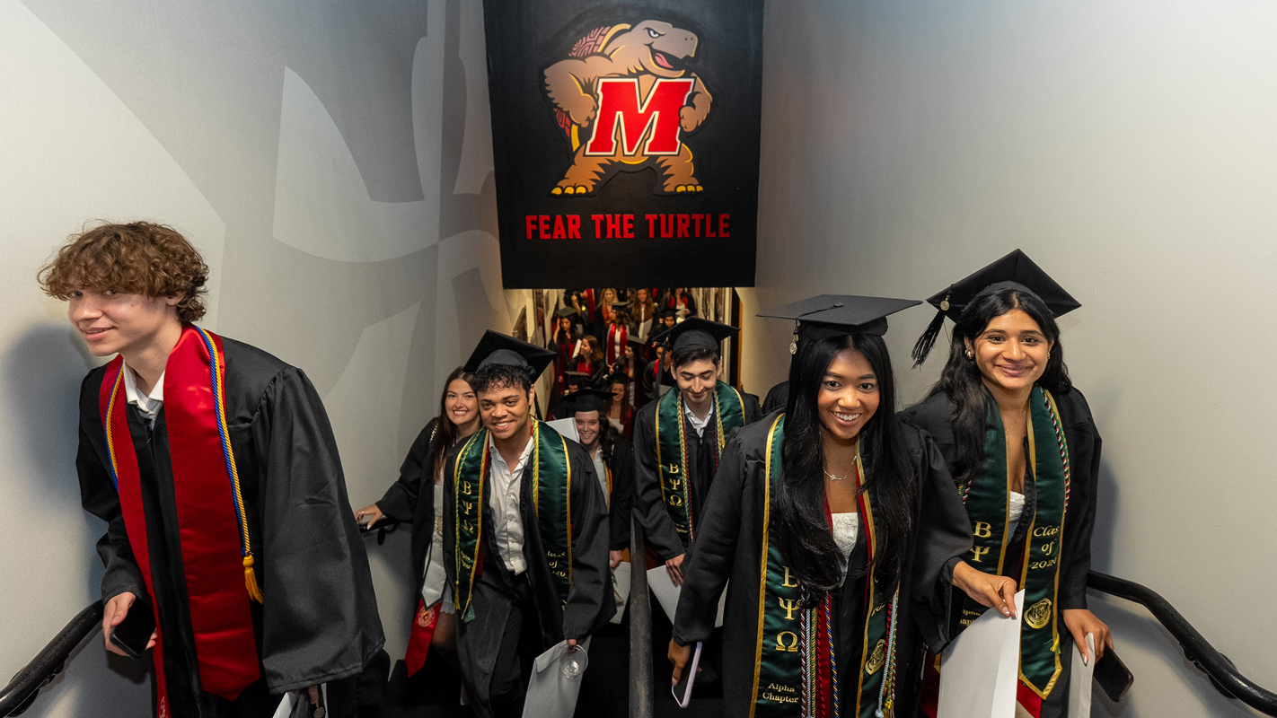 Graduates coming up stairs under a picture of Testudo, on their way to the graduation ceremony.