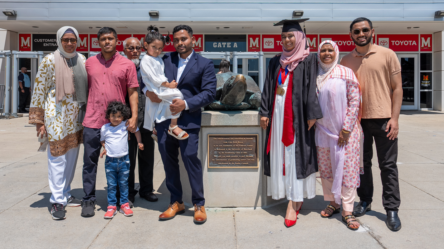 A large family with a female graduate positing with the bronze statue of Testudo outside of the Xfinity Center.