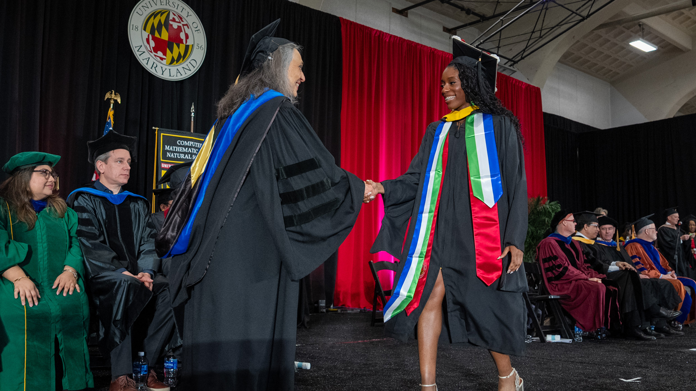A professor and master's degree recipient shaking hands on stage during the ceremony.