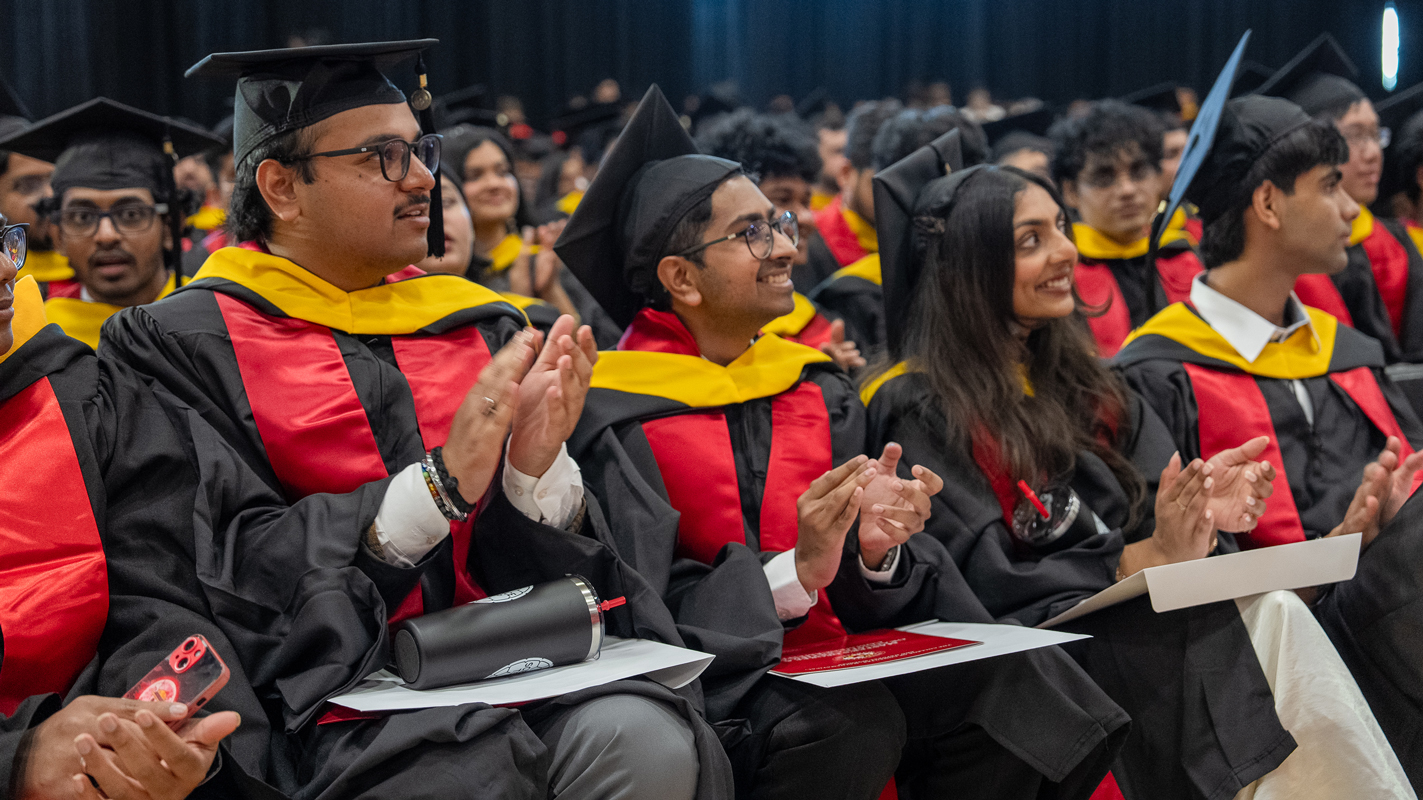 A row of master's degree students clapping during their graduation ceremony.