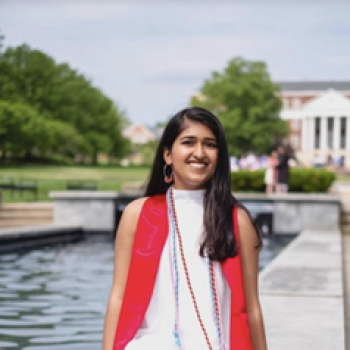 a young woman in a red vest and white dress sitting on a fountain