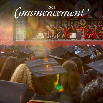 Photo of a large crowd of people at commencement. We see the students from the back, and ahead, a platform party facing the audience.