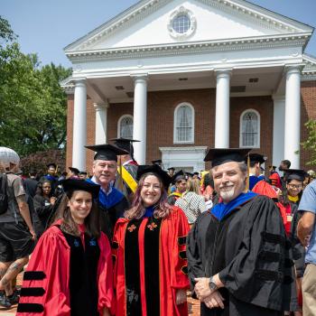 Two female Ph.D students in red regalia posing with two professors in black regalia. Credit: Lisa Helfert.