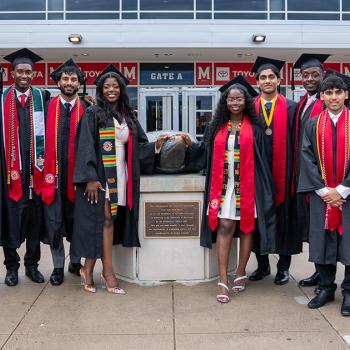 A group of graduates in regalia standing with a bronze Testudo statue. Credit: Mark Sherwood.