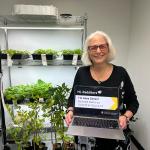 Anne Simon in front of plants holding a laptop