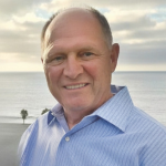 Man wearing blue button-down shirt with the ocean in the background