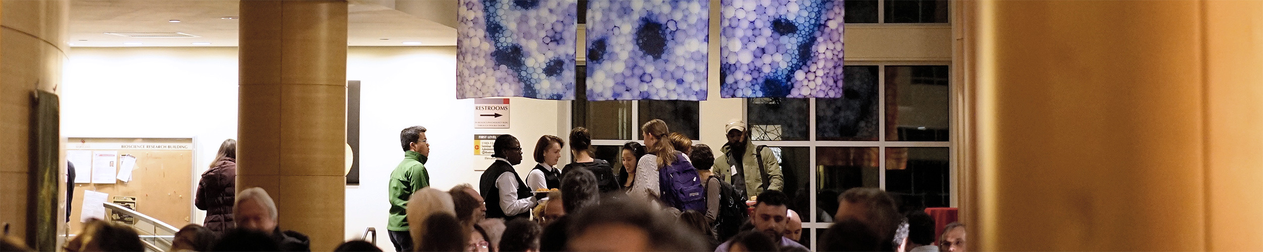 A crowd of people at an art opening for a show of microscopy art.